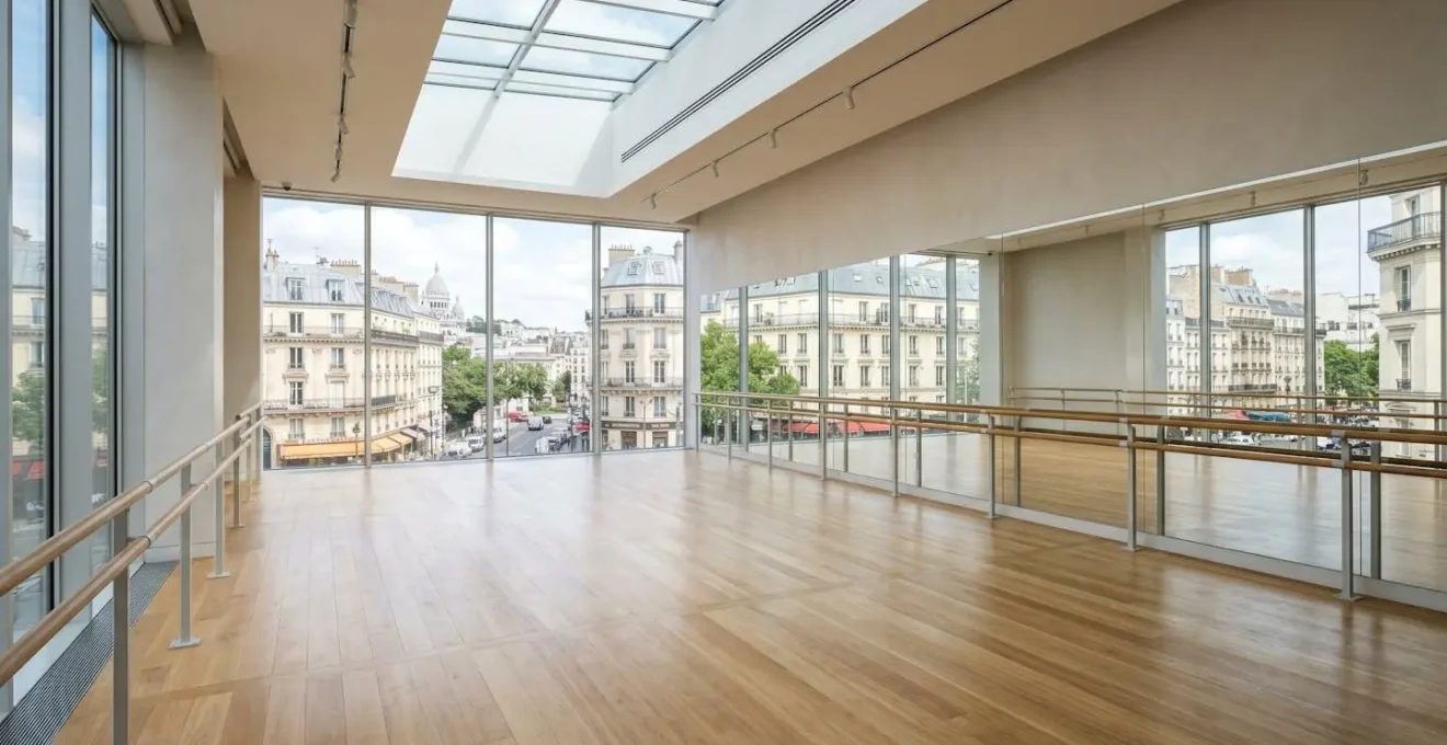 Salle de danse professionnelle moderne avec miroirs muraux, barres de travail et grandes baies vitrées donnant sur un paysage urbain français